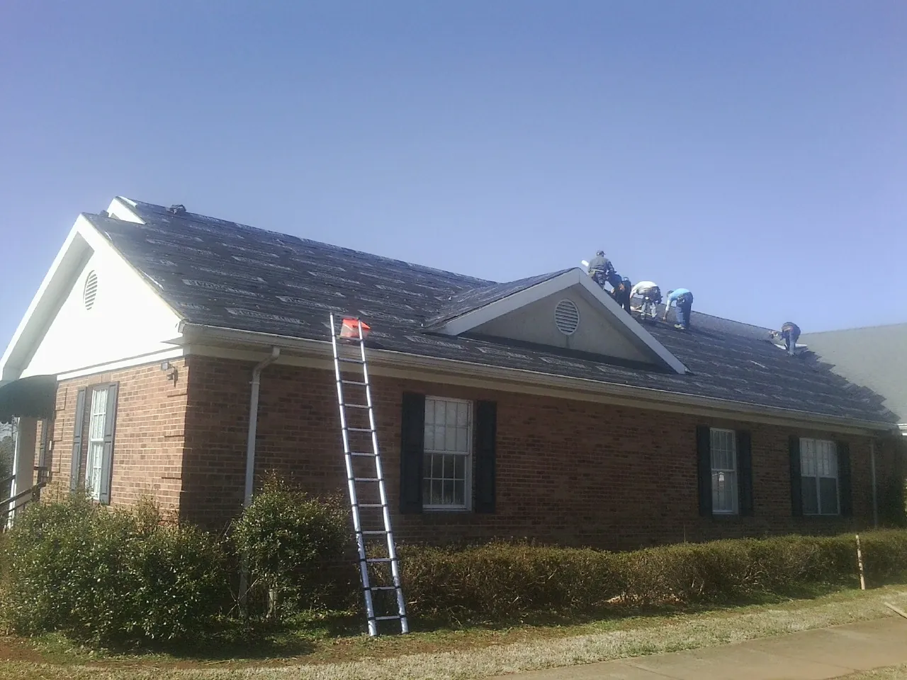 Crew tearing shingles off a brick ranch roof with a ladder set — Metal Roof Repair work by our crew in Tracy
