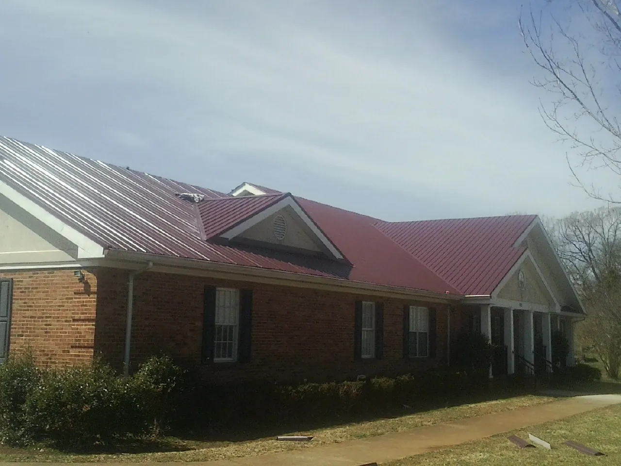 Red metal roof with gabled entries on a long brick building, from a Hail Damage Roof Repair job in Tracy
