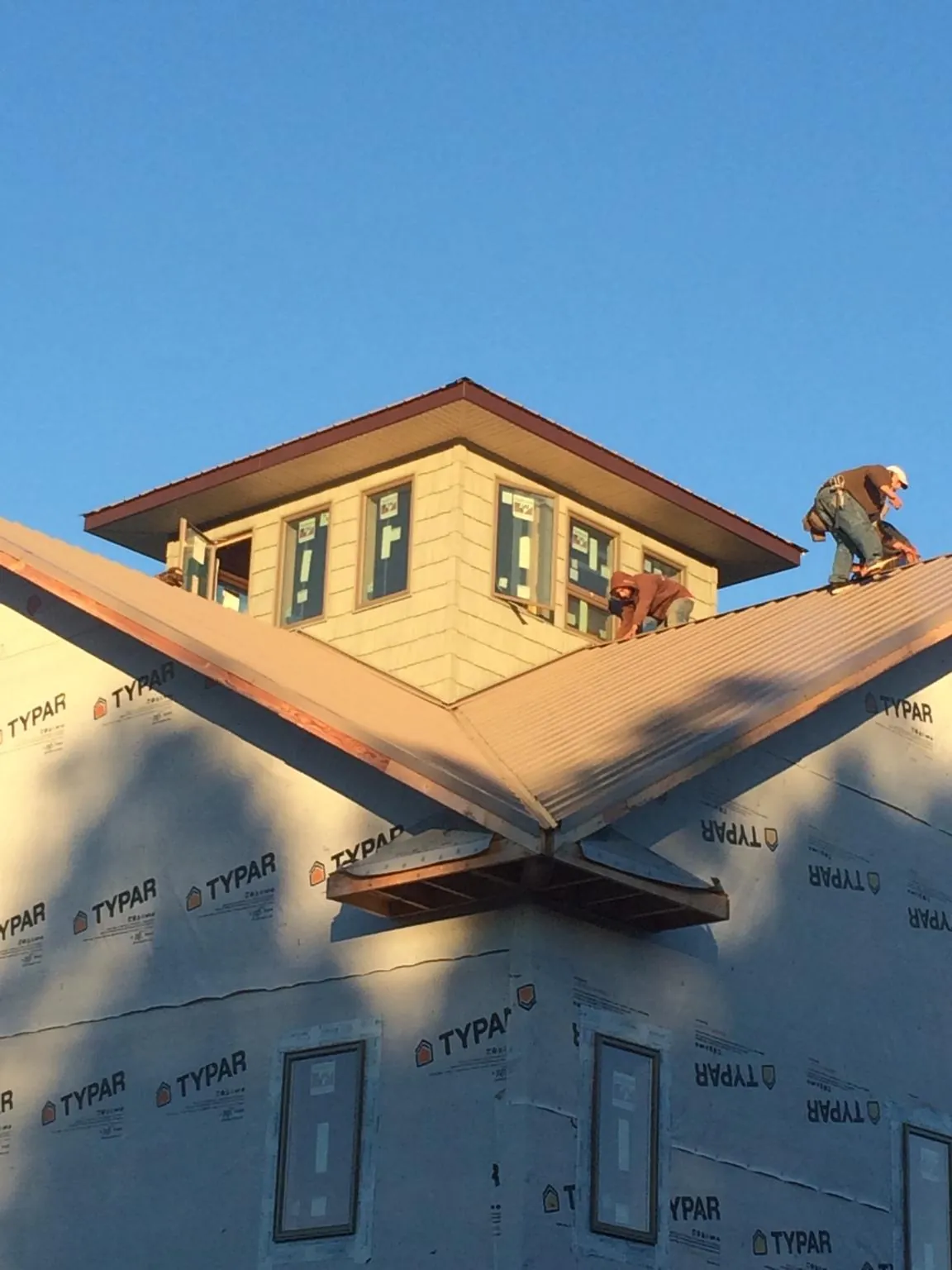 Roofers working around a rooftop cupola on a new metal roof at sunset — Roof Waterproofing in Tracy by Roofing Brothers